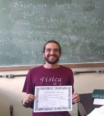 Filipe Menezes segurando o diploma em frente a um quadro-negro